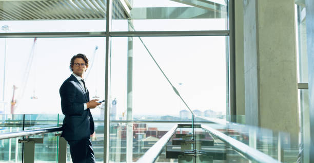 istock Businessman looking away while using mobile phone in corridor at modern office building 1166423380