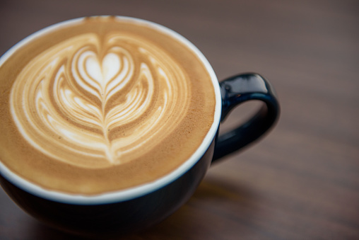 Heart shape latte art in black cup on wooden table