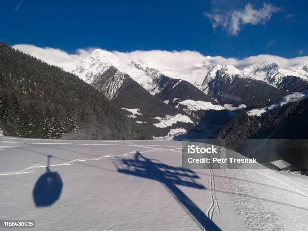 Cable Car Lift Shadow Silhouette On Fresh Snow With Aurina Valley And Mountains With Foggy Clouds On Horizon Below Blue Sky During Sunny Day In Speikboden Ski Resort In Italy Stock Photo - Download Image Now