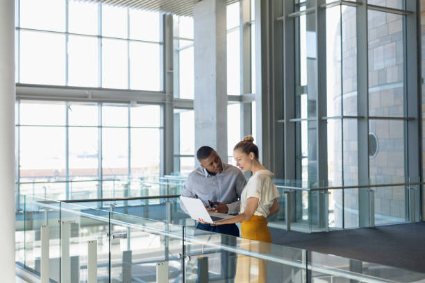 istock Two young business people stand working in modern office lobby 1166433756