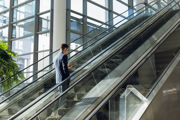 istock Businessman using phone on escalator in modern building 1166434751