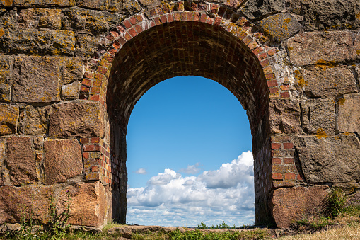 Summer view through an old medieval stone wall arched gate at Varberg Fortress in Sweden with blue cloudy sky in the background. Horizontal composition.