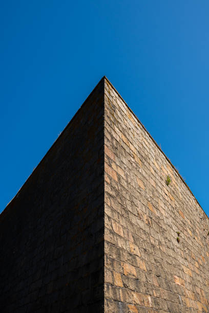 istock Closeup abstract architecture outdoors. Sharp angle of an old massive stone wall  top corner with contrast dark shadow and bright side against blue sky. 1166435183