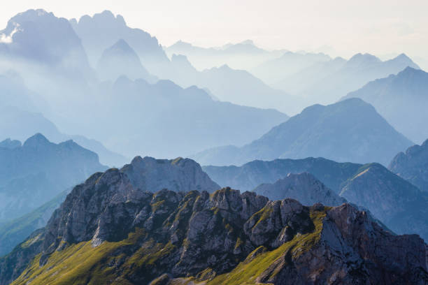 layers of silhouettes of mountain ridges and peaks in the italian alps, at sunset. view from the route down from mangart (mangrt) peak, julian alps, triglav, slovenia. - layered mountain peak summer light imagens e fotografias de stock