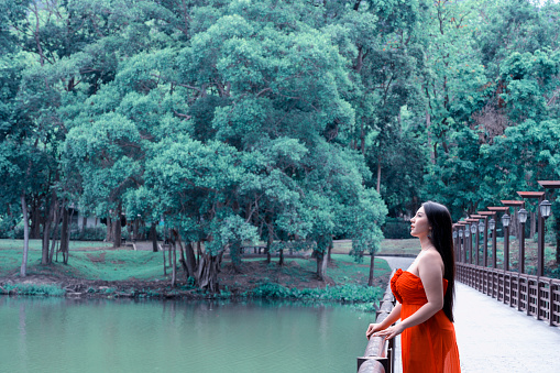 Woman in Red dress standing on the bridge look up to sky in the park