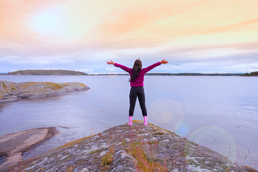 Happy freedom woman open arms to the air standing on the top of the island over colourful sky summertime in Sweden