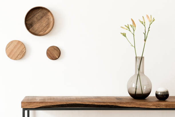 Modern and stylish concept of wooden console commode and mock up frame. Home decor. Template elegante y moderno interior de la habitación escandinava con consola de madera y anillos en la pared, hermosas flores en jarrón cristalino. composición de diseño del interior del hogar. paredes blancas, copian espacio. decoración del hogar.