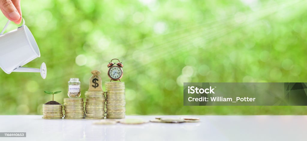 Long-tern investment, time value of money concept : Clock, US dollar bag, glass jar, a small tree on steps of rising coins. Hand pour water from a watering can, depicts asset growth from investment Investment Stock Photo