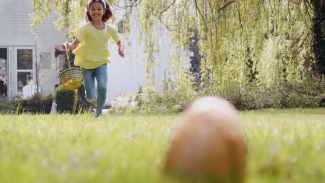 Young girl on Easter egg hunt running across garden and picking up chocolate egg to put into basket - shot in slow motion