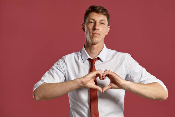 istock Young man in a classic white shirt and red tie posing over a pink background 1166442944