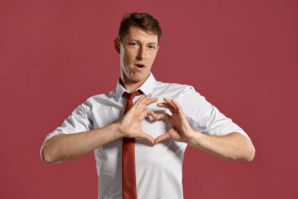 istock Young man in a classic white shirt and red tie posing over a pink background 1166443124