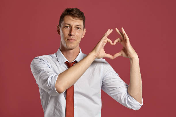 istock Young man in a classic white shirt and red tie posing over a pink background 1166443235