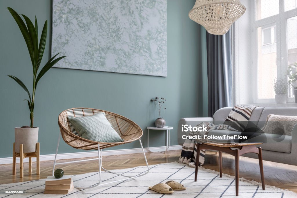 Composición moderna y bohemia de diseño interior con sofá gris, sillón rattan, reposapiés retro, a cuadros, almohada, plantas tropicales, mesa pequeña y accesorios elegantes. Decoración elegante del hogar. Plantilla. - Foto de stock de Interior libre de derechos