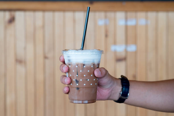 istock Iced chocolate in plastic cup in hand with wooden background 1166448860