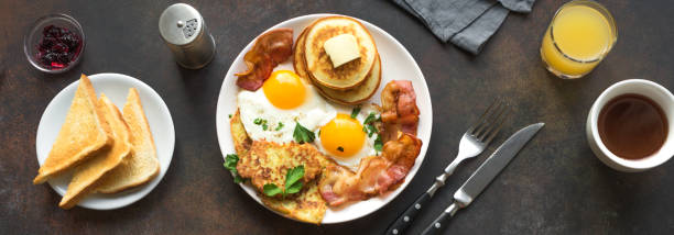 Full American Breakfast Full American Breakfast on dark, top view, banner. Sunny side fried eggs, roasted bacon, hash brown, pancakes, toasts, orange juice and coffee for breakfast. hash brown stock pictures, royalty-free photos & images