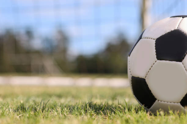 Soccer ball in goal net on grass stadium on college or high school campus. No people.  Daytime.