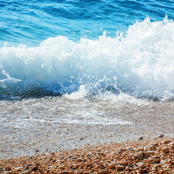 istock Breaking Wave of Blue Ocean on Pebbles beach Summer Background 1166451065