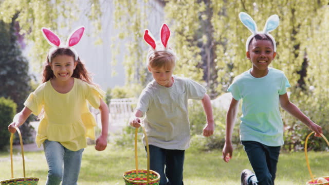 Close up of group of children wearing bunny ears on Easter egg hunt running across garden towards - shot in slow motion