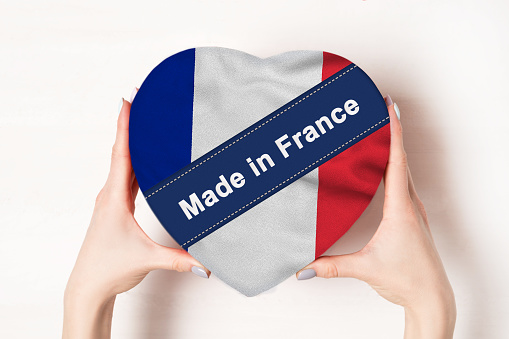 Inscription Made in France, the flag of France. Female hands holding a heart shaped box. White background. Place for text