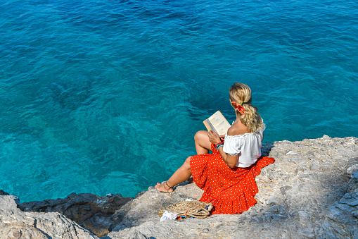Woman studying book by the sea.