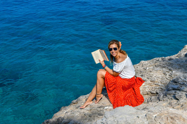 Woman studying book by the sea.