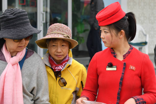 Pyongyang, North Korea - April 30, 2019: The girl, the seller of a food in uniform and senior chinese tourists. Focus on the girl