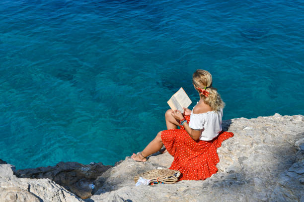 Woman studying book by the sea.