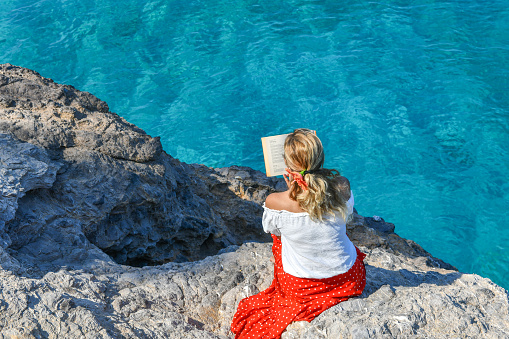 Woman studying book by the sea.