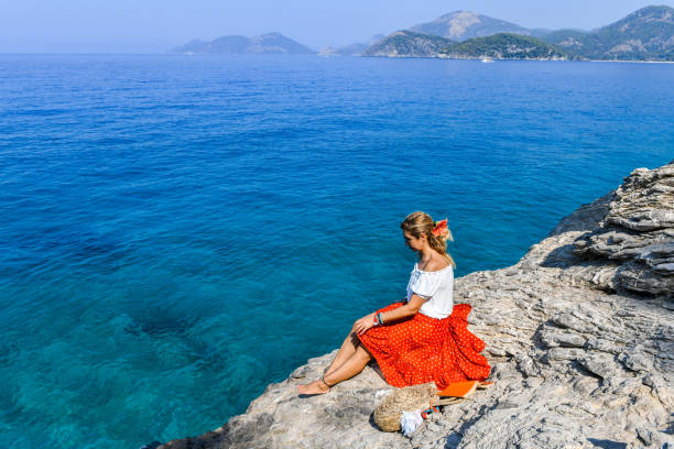 istock Woman sitting on rocks at the beach. 1166473086