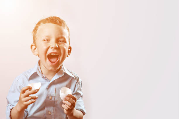 istock boy in a light shirt holding a shell from the egg and smiling on a light background 1166473163