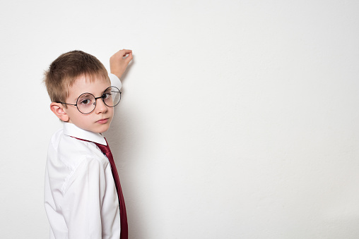 Portrait of a schoolboy in round glasses. Pretends to write on the chalkboard. White background.