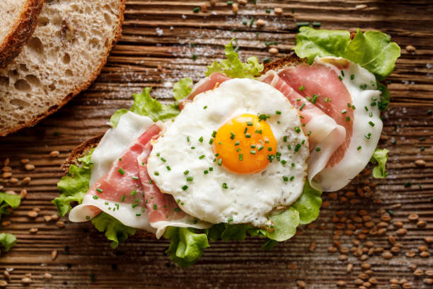 istock Sourdough bread open faced sandwich with lettuce, ham and fried egg on a rustic wooden table, top view 1166475543