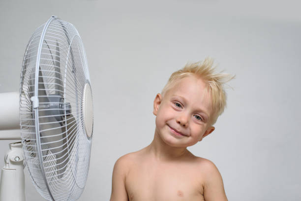 istock Pretty smiling blond boy with naked torso stands near a ventilator. Summer concept 1166476178