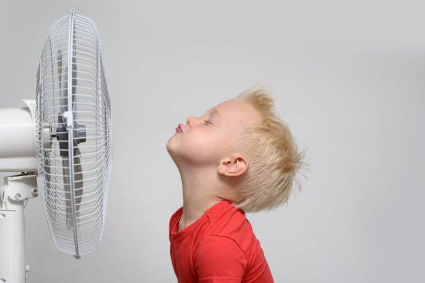 garçon blond de sourire joli dans la chemise rouge et les yeux fermés appréciant l'air frais. concept d'été - ventilateur photos et images de collection