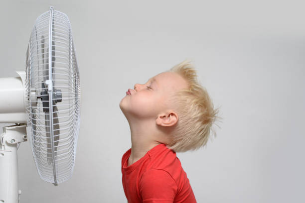 Pretty smiling blond boy in red shirt and closed eyes enjoying the cool air. Summer concept Pretty smiling blond boy in red shirt and closed eyes enjoying the cool air. Summer concept electric fan stock pictures, royalty-free photos & images