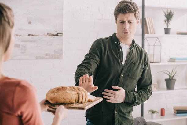 cropped view of woman holding cutting board with sliced bread near handsome man with gluten allergy stock photo