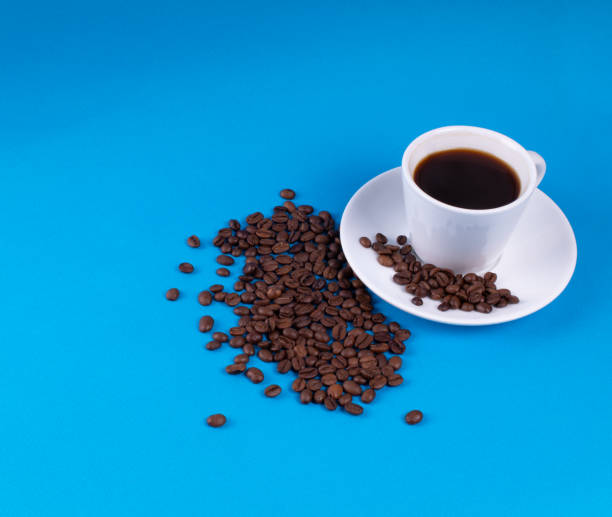 istock Spilled coffee grains after white mug on blue background 1166477359