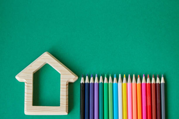 istock Wooden house figurine and several colored pencils isolate on green background, concept back to school, selective focus 1166482256