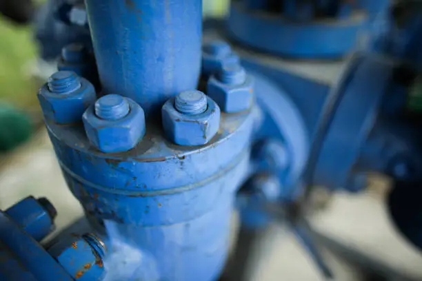 Shallow depth of field image with worn out heavy iron industrial equipment used in the oil and gas drilling industry (rusty bolts, nuts, pipes, levers)