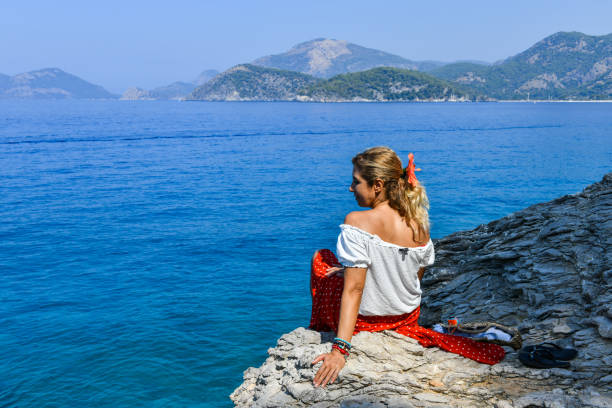 istock Woman sitting on rocks at the beach. 1166485443