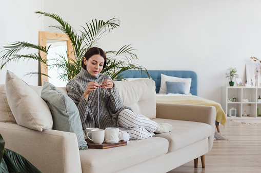 girl in a warm gray sweater knits sitting on a sofa