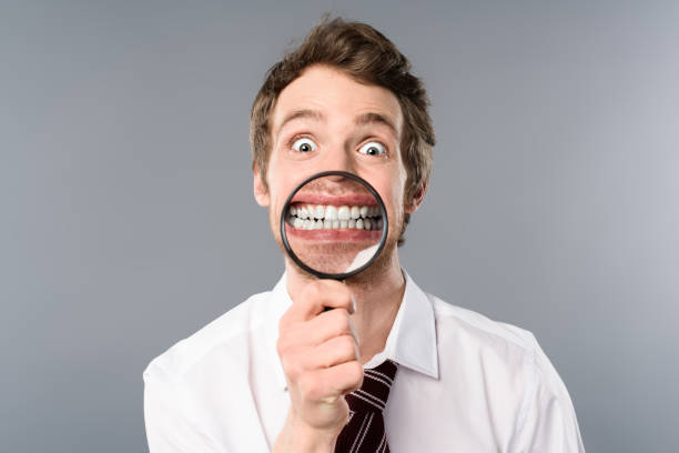 istock smiling businessman with funny face expression holding magnifier on grey background 1166496012