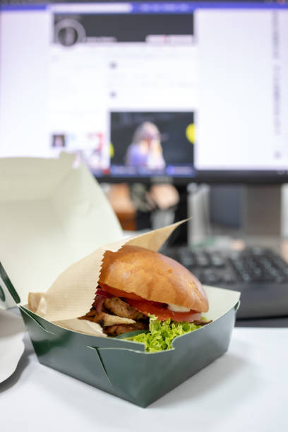istock having lunch with hamburger at workplace. desktop keyboard and display behind snack. 1166496998