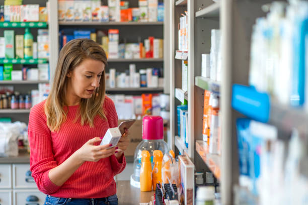 mid adult weibliche kundin, die sich in der apotheke für ein produkt entscheidet - shelf pharmacy people indoors stock-fotos und bilder