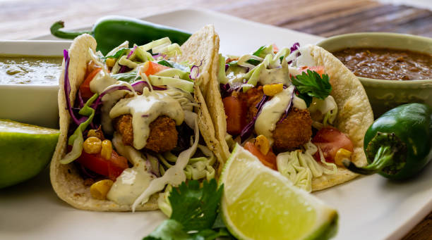 Oven-fried fish tacos with cabbage tomatoes, roasted corn and avocado-cilandro sauce Oven fried Cod fish tacos, fire-roasted salsa, toppings and salsa verde. south of the border photos stock pictures, royalty-free photos & images