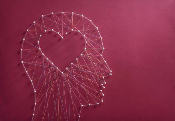 Learning to love concept. Network of pins and threads in the shape of a cut out heart inside a human head symbolising that love is the core of our being and has its own logic.