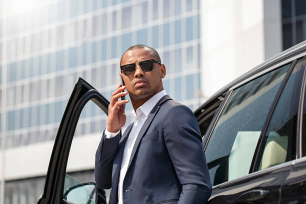 istock Young man in sunglasses leaning on car calling on smartphone looking aside serious 1166511297
