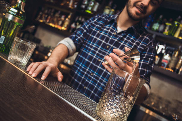 istock Young bartender standing at bar counter pouring alcohol into glass from jigger happy close-up 1166511303