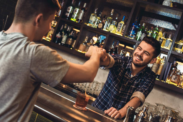 istock Young bartender standing at bar counter with customer fist bumb cheerful 1166511304
