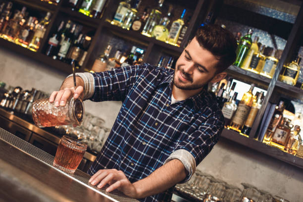 istock Young bartender standing at bar counter pouring cocktail into glass joyful 1166511308